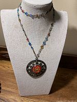 Necklace displayed on beige bust showing the medallion and beaded chain with various colors including blue, yellow, and pink beads.