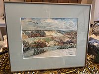 Framed watercolor painting showing a landscape with hills, trees, and sky.