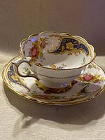 Side angle showing teacup inside saucer displaying floral and gold ornate design with scalloped edges.