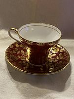 Front angle view of vintage Aynsley corset teacup with matching saucer showing red and gold chintz pattern.