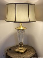 Full view of the Waterford crystal and brass table lamp illuminated, showing cream fabric shade and crystal vase body on brass base.