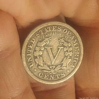 Reverse side of 1911 US 5 cent Liberty Head V nickel coin showing Roman numeral 'V' surrounded by wreath and inscriptions 'UNITED STATES OF AMERICA' and 'CENTS', held in hand.