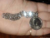 Close-up of the silver-tone chain bracelet with the 1972 Kennedy half dollar coin pendant held in palm for scale.