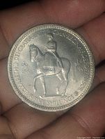 Obverse side of 1953 5 Shilling coin showing Queen Elizabeth II on horseback with inscription.