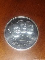 Obverse of the coin showing embossed portraits of the three Apollo 11 astronauts with their names and mission name