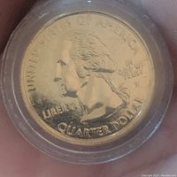 Close-up photo of the front (obverse) side of the gold plated Washington quarter coin, showing George Washington's profile, inscriptions, and protective capsule.