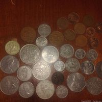 Photo showing various English coins spread out on a surface, notably silver and copper colored coins with different sizes and designs including queen profiles and heraldry