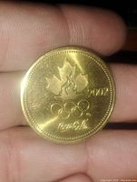 Gold-tone 2002 Winter Olympic coin with maple leaf, Olympic rings, and Coca-Cola logo.