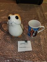 Photo showing both mugs side by side on a textured surface with lot number card.