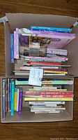 Top-down view of two boxes filled with children's books stacked horizontally and vertically, showing colorful spines and covers.