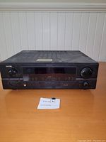 Front angle photo of the Denon DRA-397 AM/FM stereo receiver on a wooden surface, showing overall unit design and condition.