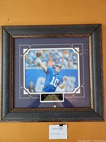 Full front view of framed poster showing Eli Manning throwing a football, with visible nameplate at bottom center.