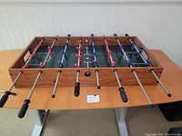 Wood framed foosball table with multiple rods and red and blue plastic players, shown from an angle.