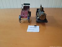 Metal vintage style car and steam locomotive train model placed side by side on a wood surface from front corner view