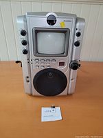 Front view of the Magnasonic KaraokeVision KR5580M karaoke machine showing the screen, control knobs, buttons, and speaker