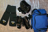 Photo showing martial arts sparring equipment including hand pads, foot pads, head gear, and a blue gym bag laid out on floor.