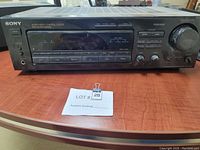 Front view of the vintage Sony STR-D565 FM Stereo Receiver showing buttons, digital display panel, and power knob on a wooden surface with auction lot tags.