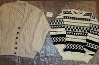 Full view of two vintage sweaters side by side; one black and white patterned crewneck and one cream button-down cardigan.