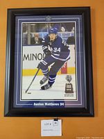 Framed poster of Auston Matthews skating in Toronto Maple Leafs uniform with Calder Trophy image and award text, mounted with double mat and black frame