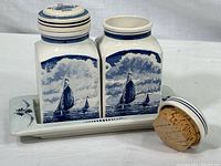 Front and side view of two ceramic canisters with hand painted sailing ship motif and cork stopper, sitting on a tray.