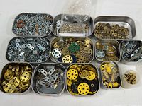 Multiple small lidded metal boxes containing various nuts, bolts, washers, metal gears, and plastic fittings organized inside a larger storage box.