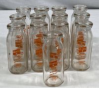 Thirteen clear glass milk bottles arranged in rows showing orange Cloverleaf Farms label.