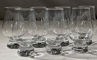 Seven clear Glencairn whisky glasses grouped together on a white surface highlighting their tulip shape and short base.