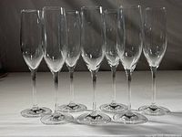 Seven clear champagne flute glasses arranged in a row, showing stems and bowls clearly.