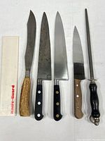 Top-down view of all knives and sharpening steel laid out on white surface