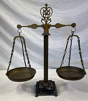 Front view of entire brass balance scale including two pans, twisted column, ornate beam, and marble base