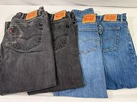 Four pairs of Levi's jeans folded side by side, two black/dark gray washes on left and two blue washes on right, showing overall lot contents.