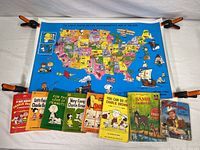 Six Peanuts paperback books and two older children's books (Bambi, Roy Rogers) laid out beneath a colorful Peanuts-themed MetLife map of the United States.