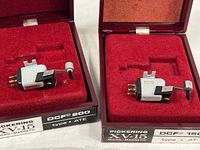 Two Pickering XV-15 micro-magnetic cartridges in original red felt-lined storage boxes. Each cartridge sits recessed in foam padding inside maroon cases labeled DCF 200 type ATE and DCF 150 type AT.