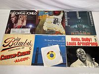 Photo showing seven vintage 45 RPM vinyl record singles by George Jones, Rory Gallagher, Electric Light Orchestra, Cheech & Chong, Louis Armstrong, George Shearing, and Stevie Wonder arranged on a white surface.