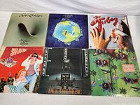 Collection of 7 vintage vinyl records arranged on a white surface, showcasing album cover art by Robin Trower, Yes, The Tubes, Sha Na Na, Electric Light Orchestra, and Cecilio and Kapono