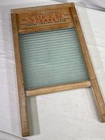 Full view of the vintage white wood washboard with glass scrubbing surface lying flat on a white cloth background.