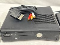 Black Xbox 360 console front view with power button and composite AV cable placed on top