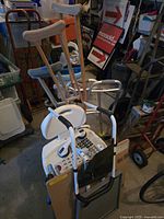 Wooden crutches, white bath seat, white walker, and large black rotary dial telephones in a dimly lit storage area
