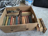 Box filled with approximately 30 assorted antique and vintage hardcover books with varied colors and bindings.