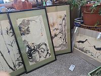 Four framed Asian paintings displayed leaning against seating and plants