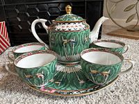 Full view of the porcelain tea set displaying teapot, teacups, and platter with green leaf and dragonfly pattern