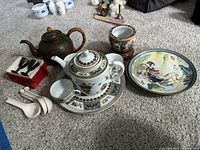 The full lot spread showing metal teapot, ceramic teapot with lid, white soup spoons, two Asian plates, two carved stone cups, and planter with stand.
