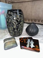 Lot showing large black ceramic vase with intricate gold Asian-inspired etching, smaller black ribbed vase, and two square mother of pearl inlaid coasters on floor.