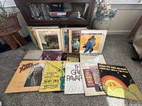 Assorted vinyl albums arranged on floor near bookcase and large vase.