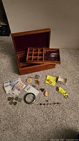 Collection of assorted jewelry and currency displayed around a wooden jewelry box with removable tray