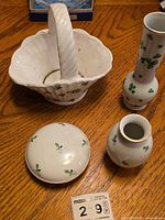 White ceramic basket with handle, two vases, and lidded bowl displaying the green leaf pattern on a wooden table