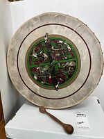 Front view of round wooden framed bodhran drum with goatskin head showing Celtic circle design and included wooden tipper beater in front.