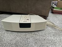 Front view of beige Bose Wave Radio on carpet, showing front speaker grille and digital display.