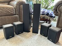 Six Cambridge SoundWorks speakers; four small satellites and two tall towers positioned on carpet in living room.