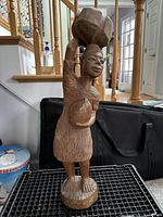 Front-side view of the wooden figurine showing the woman's face, basket on head, and jug in hand.